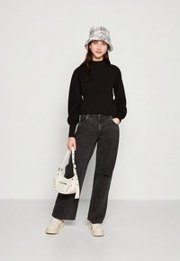 Top preto de manga comprida, jeans cinzentos de pernas largas com um rasgo, chapéu tipo balde creme e mala branca com ferragens decorativas. Sapatos plataforma bejes grossos.