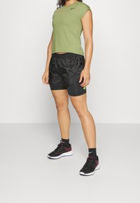 Camiseta atlética de manga corta verde, pantalones cortos negros y zapatillas negras con acentos en burdeos. Presenta el logo de Nike en la camiseta y en los pantalones cortos.