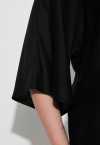 Top nero a maniche corte con un design fluido. Il tessuto appare morbido con una superficie leggermente texturizzata. Presenta maniche larghe e scivolose.