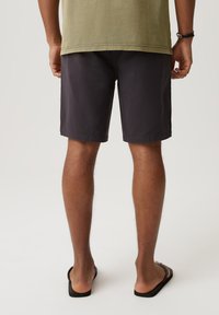 Ciemnoszare szorty o prostym kroju, wykonane z lekkiego materiału, z gładkim wzorem i bocznymi kieszeniami. Widziane czarne klapki.