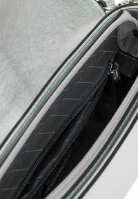Sac à main synthétique argenté avec un extérieur texturé. L'intérieur dispose de deux compartiments zippés et d'une doublure grise, offrant un rangement organisé.
