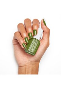 Groene nagellak in een transparante glazen fles met een witte dop, vastgehouden tussen vingers met een bijpassende groene manicure. Glad, glanzend afwerking.