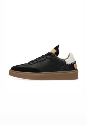 Black low-top sneaker with tan sole, white heel accent, stitching details, and black laces, displayed on a white background.