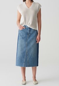 Haut en maille à manches courtes de couleur crème, associé à une jupe en denim bleu moyen avec une couture centrale et un ourlet brut. Modèle portant des ballerines de couleur neutre.