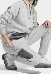 Grå sweatshirt med huva, utrustad med en mörkgrå ficka och justerbara dragsko. Kompletterad med grå sweatpants som har en ficka med dragkedja.