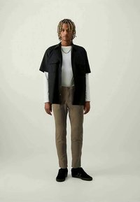 Svart kortärmad tröja över en vit långärmad tröja, beige byxor och svarta sneakers. Ledig stil med två bröstfickor.