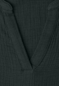 Gros plan sur un tissu gris foncé texturé avec un col en V profond et des coutures visibles le long des bords.
