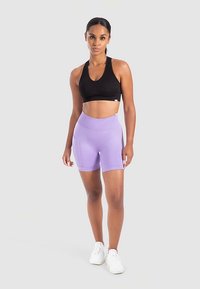 Zwarte sportbeha en lichtpaarse short met hoge taille, gemaakt van rekbare stof met zijzakken, gecombineerd met witte sportschoenen.