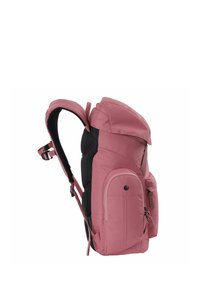 Mochila de tela rosa con respaldo y correas acolchadas, múltiples bolsillos y una parte superior redondeada. Textura suave con acentos en negro contrastantes.