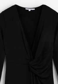 Robe noire avec un décolleté en V profond et des manches longues. Présente des détails froncés à la taille, fabriquée à partir d'un tissu lisse et extensible.