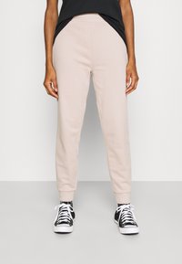 Helle beige Sweatpants mit elastischem Bund, seitlichen Taschen und gerippten Bündchen, kombiniert mit schwarz-weißen Sneakern. Glatte Textur.