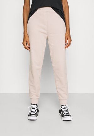 Ljusbeiga sweatpants med elastisk midja, sidfickor och ribbade muddar, parat med svarta och vita sneakers. Slät textur.