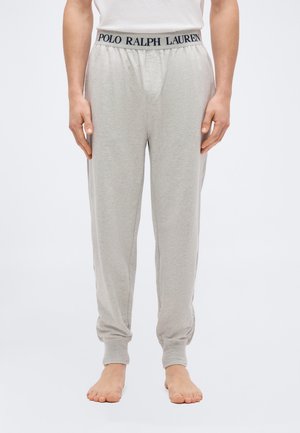 Pantalon de jogging gris clair avec poignets et ceinture élastiques, portant l'inscription "Polo Ralph Lauren", porté par une personne pieds nus immobile.