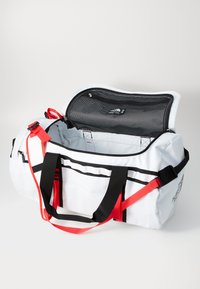 White duffle bag with black accents and red straps, featuring a large opening, zipper closure, and inner mesh pocket for organization.