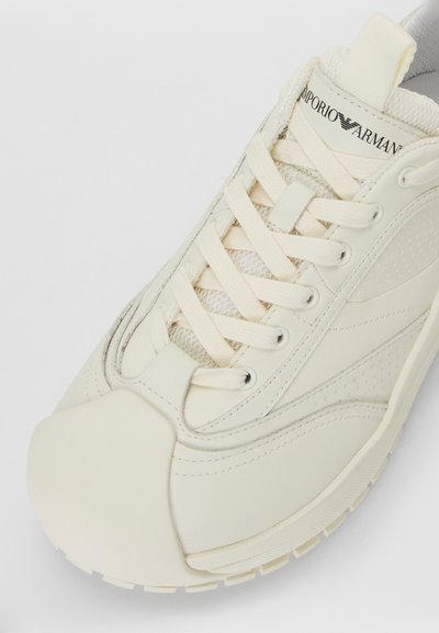Kreemik valge Emporio Armani tennisekenks, millel on pehmendatud keeleosa, lame paelad, kummist tald ja tekstureeritud sünteetiline ülemine osa.