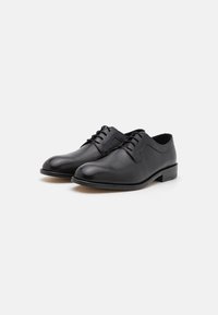 Black leather dress shoes with a polished finish, rounded toes, and lace-up design; featuring a low stacked heel and minimal stitching detail.