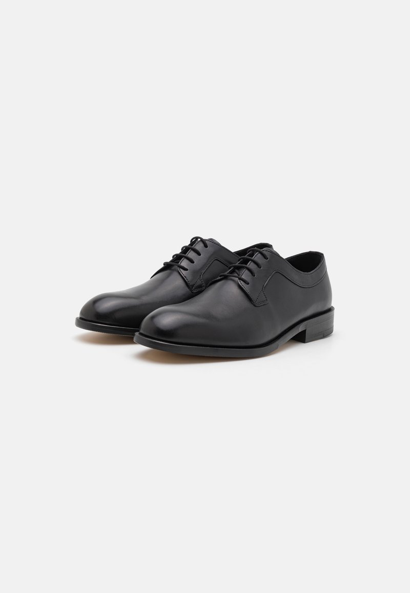 Chaussures de ville en cuir noir avec une finition brillante, des bouts ronds et un design à lacets ; dotées d'un petit talon empilé et de détails de couture minimalistes.