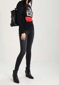 Sudadera negra con texto en blanco y rojo, jeans ajustados negros y botines negros con tacón en cuña. Mochila de cuero negro.
