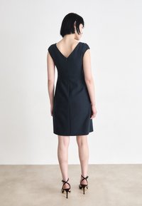 Dark navy dress with a V-back and short sleeves, tailored fit, featuring a center back zipper, complemented by strappy black high heels.