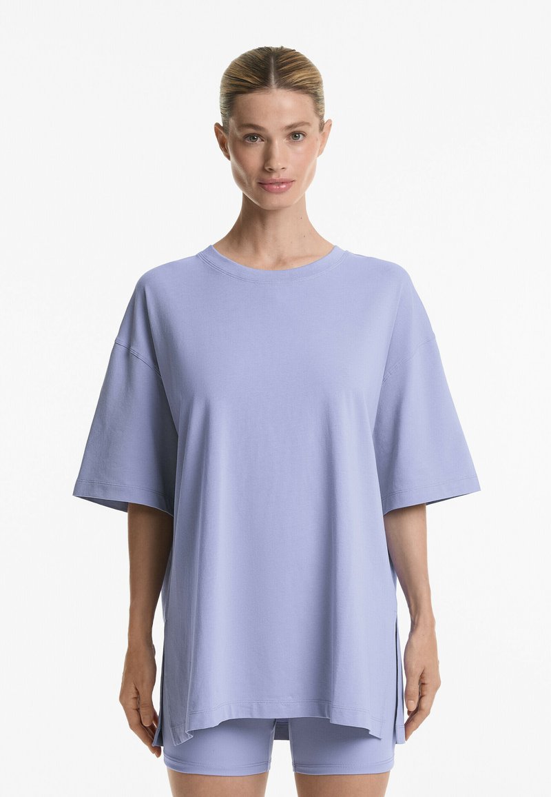 Světle fialové oversized tričko vyrobené z měkké látky, má krátké rukávy, kulatý výstřih a volný střih s bočními rozparky.