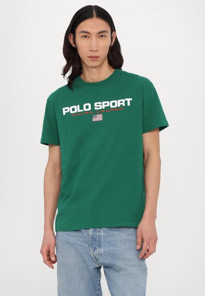 Camiseta de algodón verde con cuello redondo y mangas cortas, que presenta el texto "POLO SPORT" en blanco y rojo, además de un gráfico de la bandera americana.