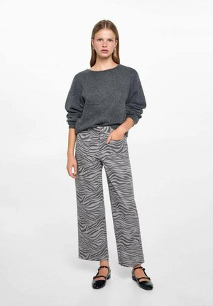 Szary, oversize sweter z długimi rękawami, w zestawieniu z szerokimi spodniami w szary zebra i czarnymi płaskimi butami. Gładkie tekstury i luźny krój.