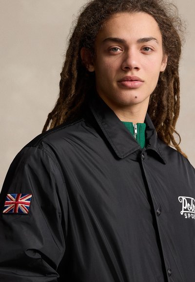 Schwarze Zip-Jacke mit einem knöpfbaren Kragen, "Polo Sport"-Logo, grünen Reisverschlussdetails und einer gestickten Union Jack auf der Schulter.