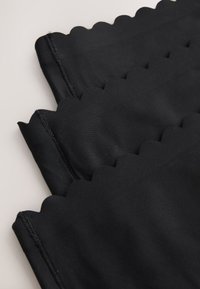 Tissu noir aux bords festonnés, plié et superposé, montrant une texture lisse et des coutures cousues sur un fond clair.