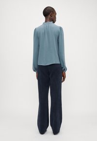 Lichtblauwe blouse met lange mouwen, een gerimpelde kraag en pofmouwen, gecombineerd met donkerblauwe, wijde broekspijpen. Soepele textuur, ontspannen pasvorm.