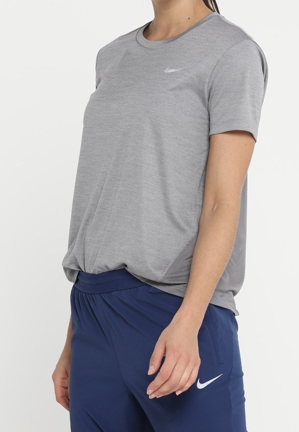 Camiseta deportiva gris de manga corta con cuello redondo y un sutil logo de Nike en el pecho, combinada con pantalones cortos deportivos azul marino con logo.