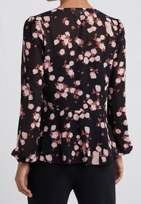 Blusa negra con mangas largas y abullonadas, diseño peplum, con un patrón floral de rosas en tonos rosa claro y blanco sobre una tela translúcida.