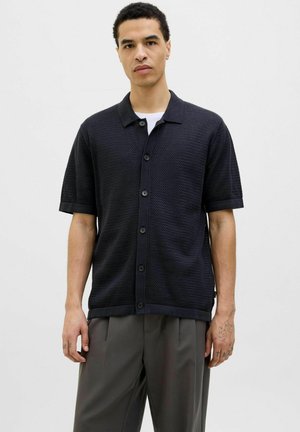 Chemise boutonnée à manches courtes bleu marine foncé avec un motif en tricot texturé et des finitions contrastées. Elle présente un col classique et des boutons sur le devant.