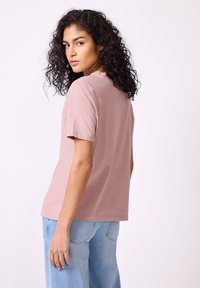 T-shirt med kort ärm och rund halsringning i mjuk pastellrosa bomull, kombinerad med ljusblå jeans i löst snitt. Enkel design utan synliga mönster.
