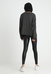 Svart- och vitrandig oversized tröja med rund halsringning, i kombination med svarta leggings och vita sneakers, sedd bakifrån.