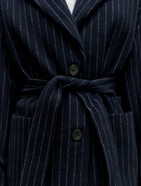 Marine gestreepte jas van zacht materiaal, met een sjawlkragen, twee voorknosjes, een strikceintuur en zwarte knopen voor de sluiting.