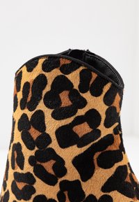 Kotníkové boty s leopardským vzorem z texturovaného, měkkého materiálu. Černobéžový vzor s hladkým černým okrajem kolem horního otvoru.