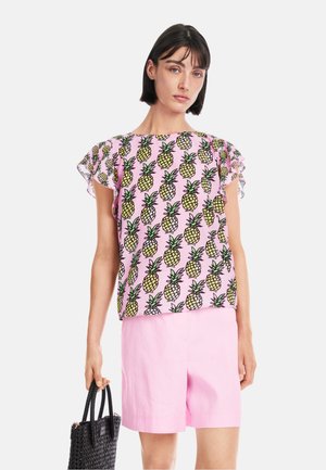 Pink blouse with pineapple print, short ruffled sleeves, paired with pink shorts and a black woven handbag. Smooth, lightweight fabric.