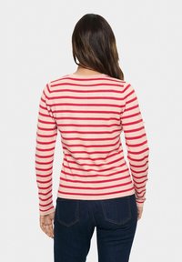 Langärmeliges Hemd mit roten und cremefarbenen horizontalen Streifen, Rundhalsausschnitt und figurbetontem Schnitt, kombiniert mit dunklen Jeans aus Denim.
