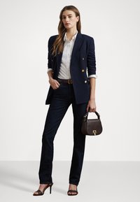 Námořnický dvojitě zapínaný blazer, bílá košile s knoflíky, tmavé džíny, hnědá kabelka se zlatými akcenty a černé otevřené podpatky.