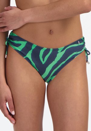 Žena v zelených a tmavě modrých vzorovaných spodních dílech bikin se zavazováním na bocích, viditelný trup a horní část stehen.