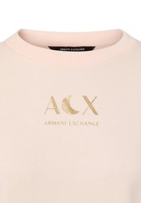 Sweatshirt rose clair avec col rond côtelé. Orné d'un logo doré "ACX" et du texte "ARMANI EXCHANGE" imprimé en dessous.