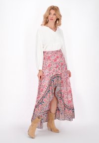 Langer blumiger Rock in Pink mit asymmetrischem Saum und dekorativem Rand. Kombiniert mit einem weißen Langarmoberteil und beigen Ankle Boots.