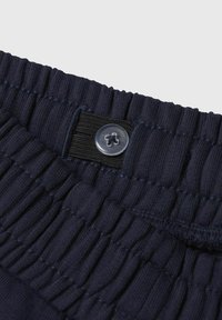 Ceinture élastique bleu marine avec texture froncée, dotée d'un fermoir à bouton transparent. Le tissu semble doux et extensible.