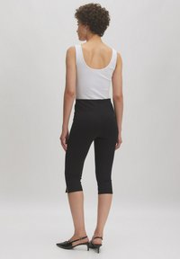 Zwarte, fitted capri broeken met zijsplitten, gecombineerd met een witte tanktop. Heeft een gladde textuur en een hoge taille.