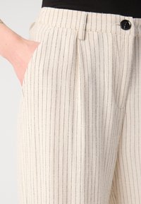 Beige gestreifte Hose aus leichtem Stoff, mit einem gefältelten Design, seitlichen Taschen und einem schwarzen Knopfverschluss.