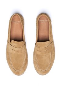 Mocasines de ante en color marrón claro con un diseño de estilo mocasín, que presentan detalles de costura y un acabado suave y texturizado. Suela plana con una elevación mínima.