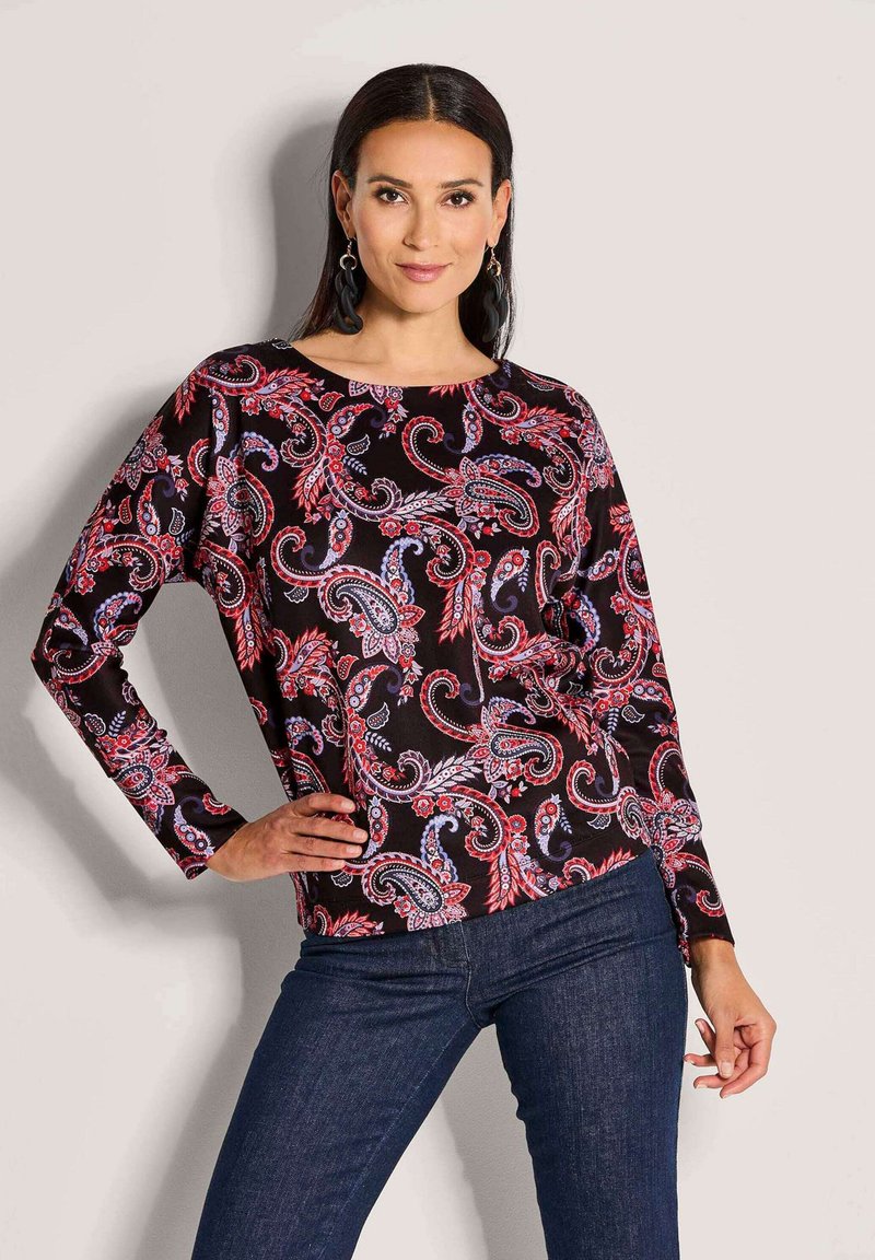 Langärmliges Oberteil aus schwarzem Stoff mit einem lebhaften rot-blauen Paisleymuster. Runder Ausschnitt und lockere Passform. Kombiniert mit dunklem Denim.