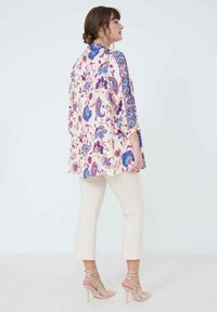 Floral-patterned lightweight tunic in cream, featuring vibrant blue, pink, and green designs, with 3/4 sleeves and a loose fit, paired with white cropped pants.
