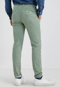Lichtgroene corduroy broek met een slim fit, voorzien van twee achterzakken met gouden hardware, opgerolde mouwen, en gestyled met witte sneakers.