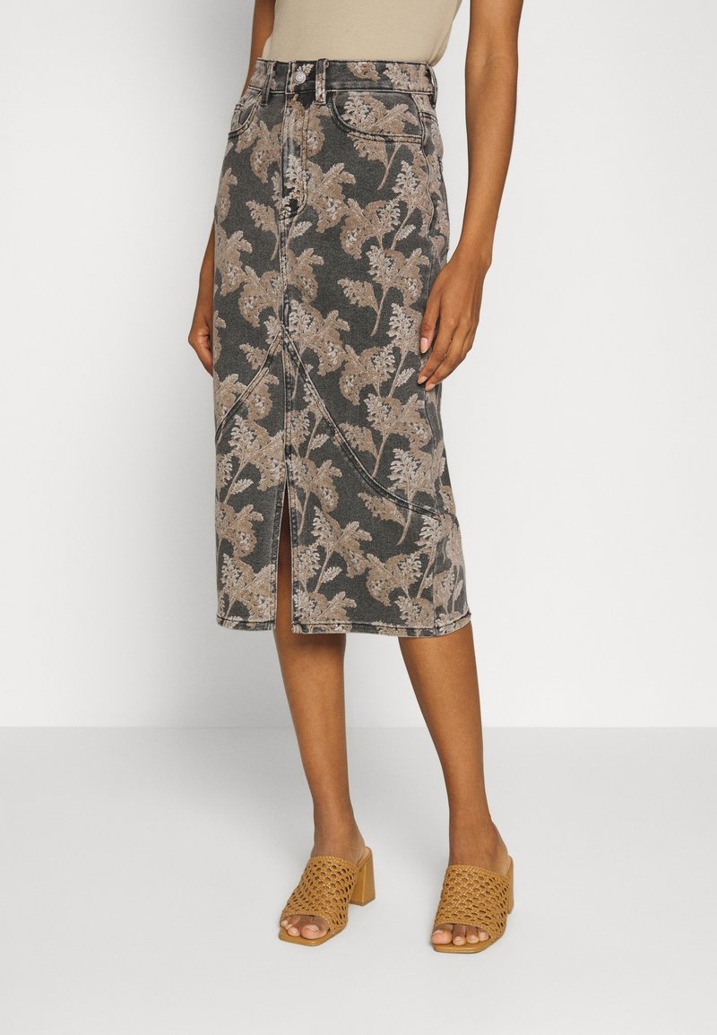 Femme portant une jupe taille haute, longueur genou, avec un imprimé floral beige et une fente à l'avant, associée à des sandales à talons tressées couleur sable.
